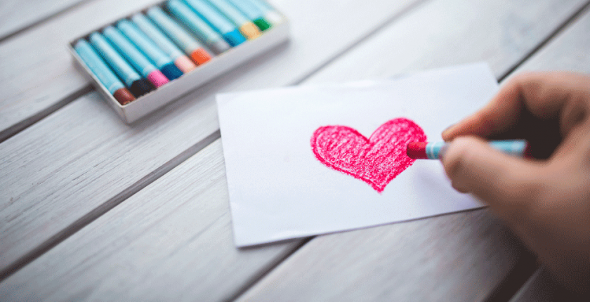 A hand drawing a love heart with crayons