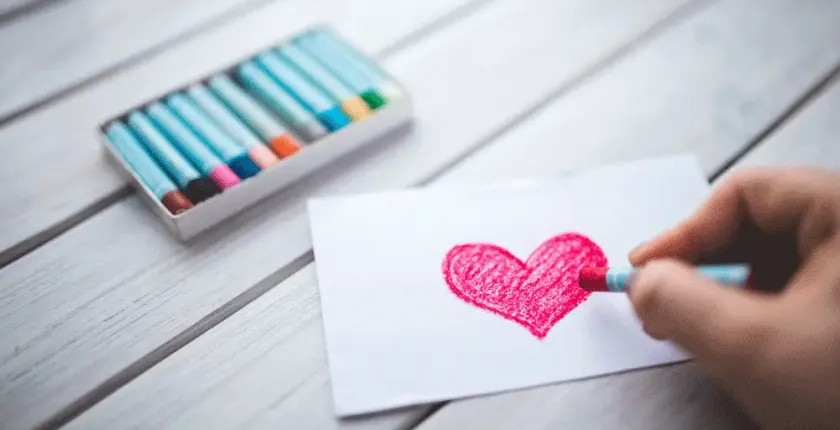 A hand drawing a love heart with crayons